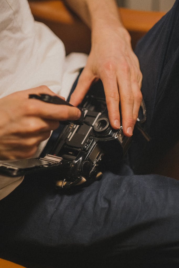 A close-up of a person fixing a vintage camera indoors.